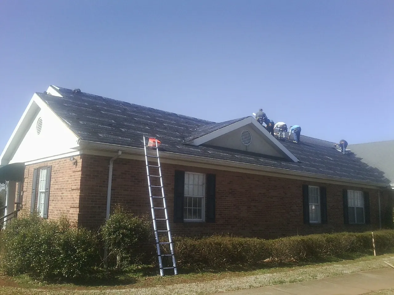 Crew tearing shingles off a brick ranch roof with a ladder set — Metal Roof Repair work by our crew in Macungie