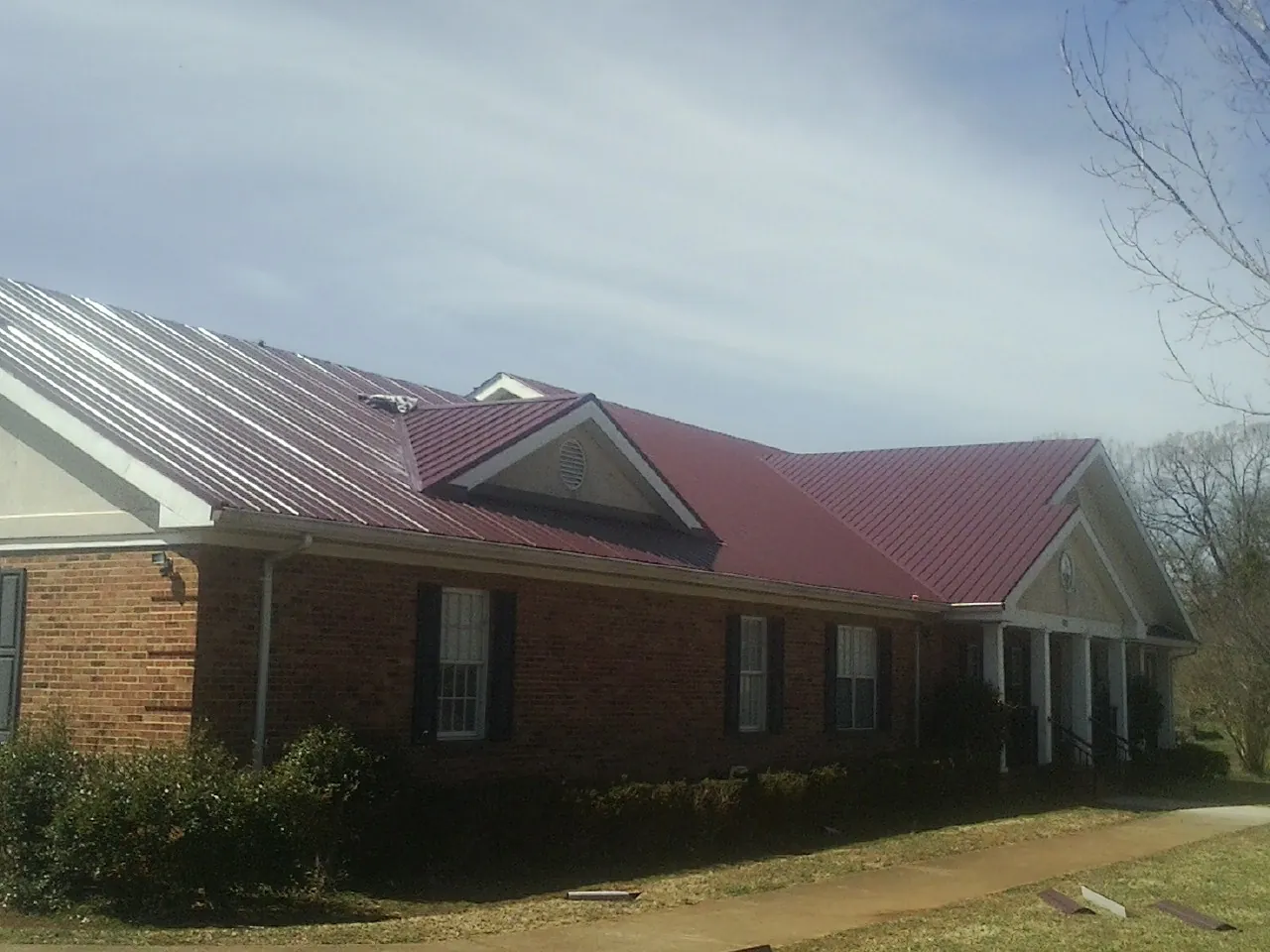 Red metal roof with gabled entries on a long brick building, from a Hail Damage Roof Repair job in Macungie