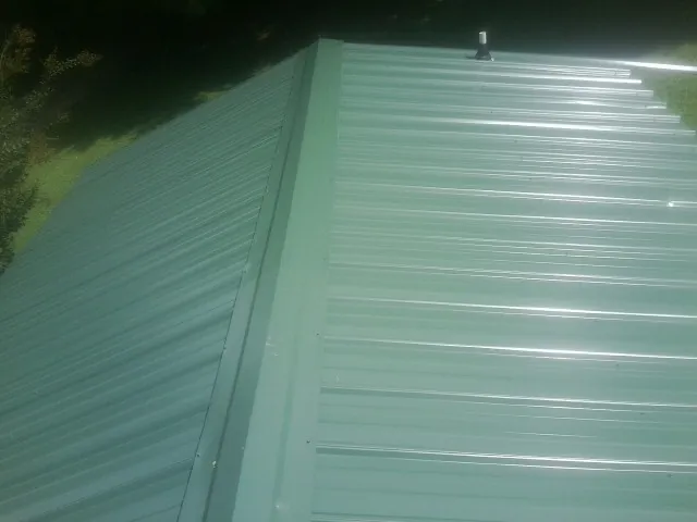 New green metal panels meeting at the ridge of a roof — Flat Roof Repair work by our crew in Macungie