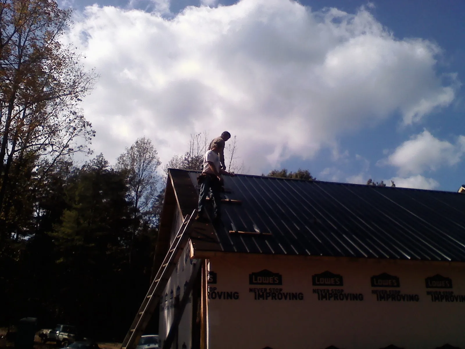 Roofer fastening dark metal panels high against a cloudy sky, from a Roof Inspection job in Macungie