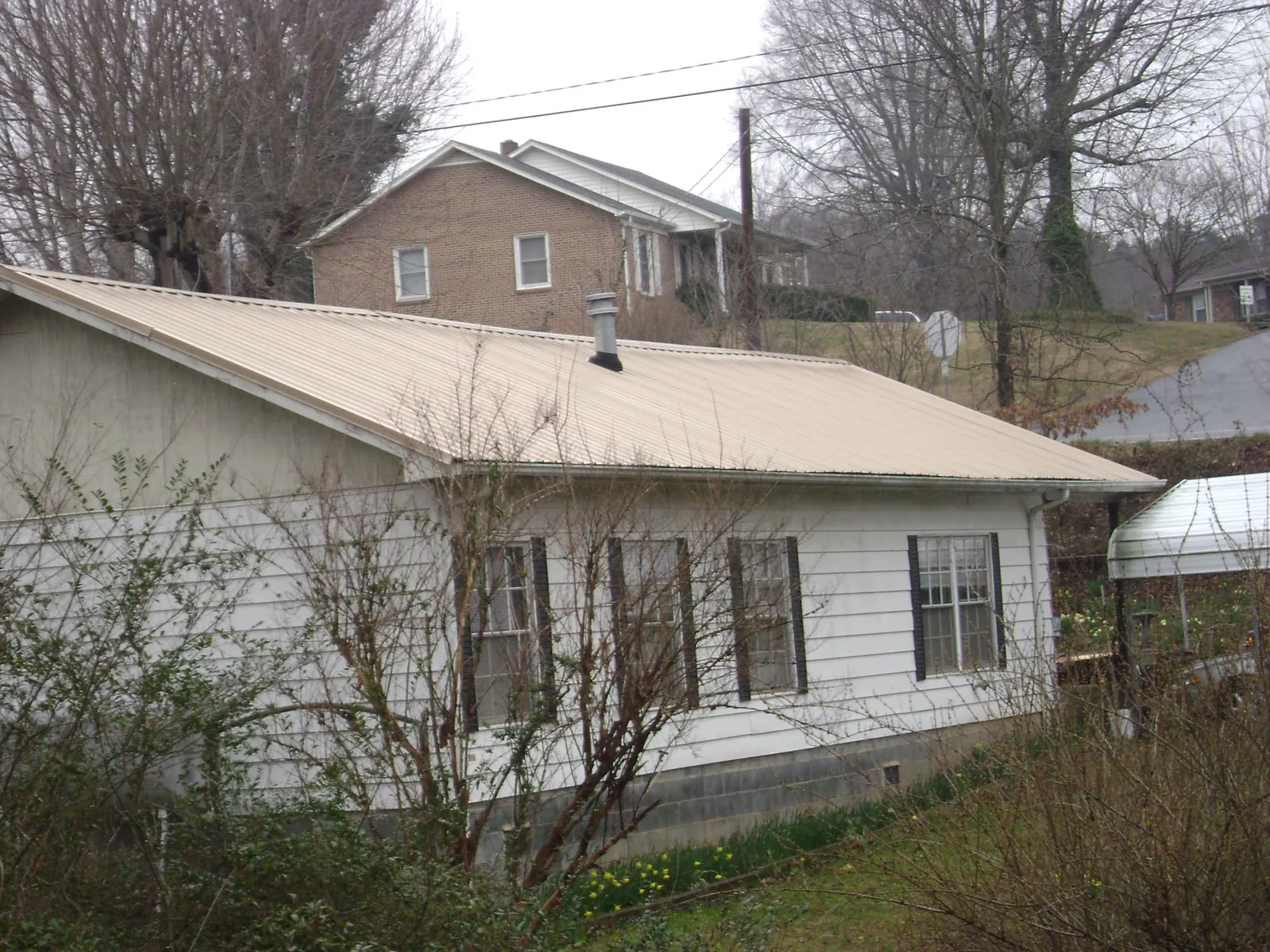 Tan metal roof on a white sided house set into a hillside — Commercial Roofing by Roofing Brothers in Macungie